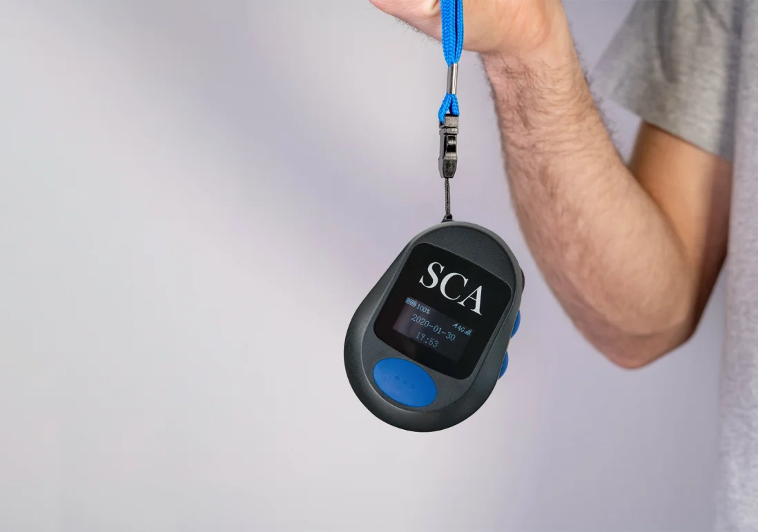 A hand holding a SafeTCard wearable duress button